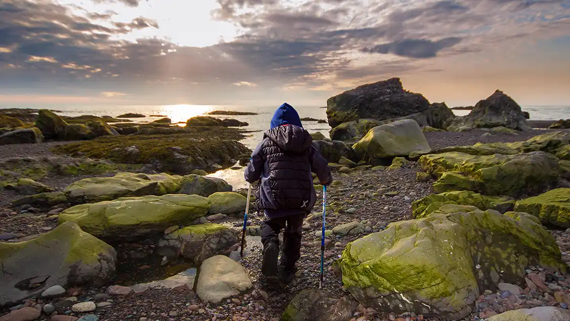 A young boy in outdoor wear hiking the Green Gardens Trail in Gros Morne National Park toward the ocean