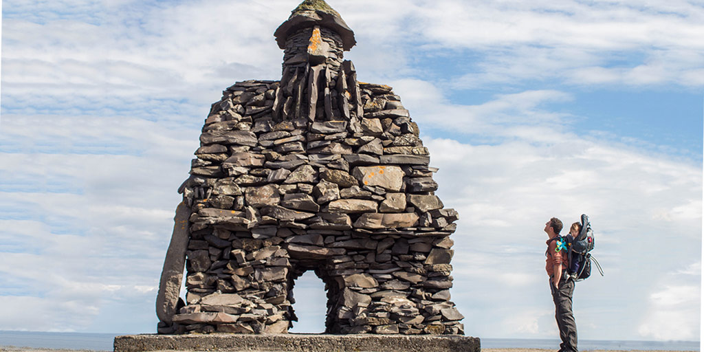 A father and son stare up at an Icelandic sculpture on the coast