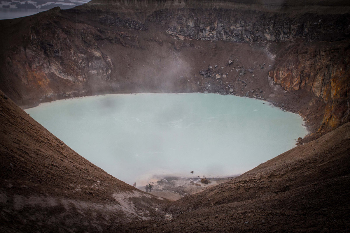 A group of people hike down to a volcanic crater with milky white water - An Epic 14 Day Iceland Itinerary