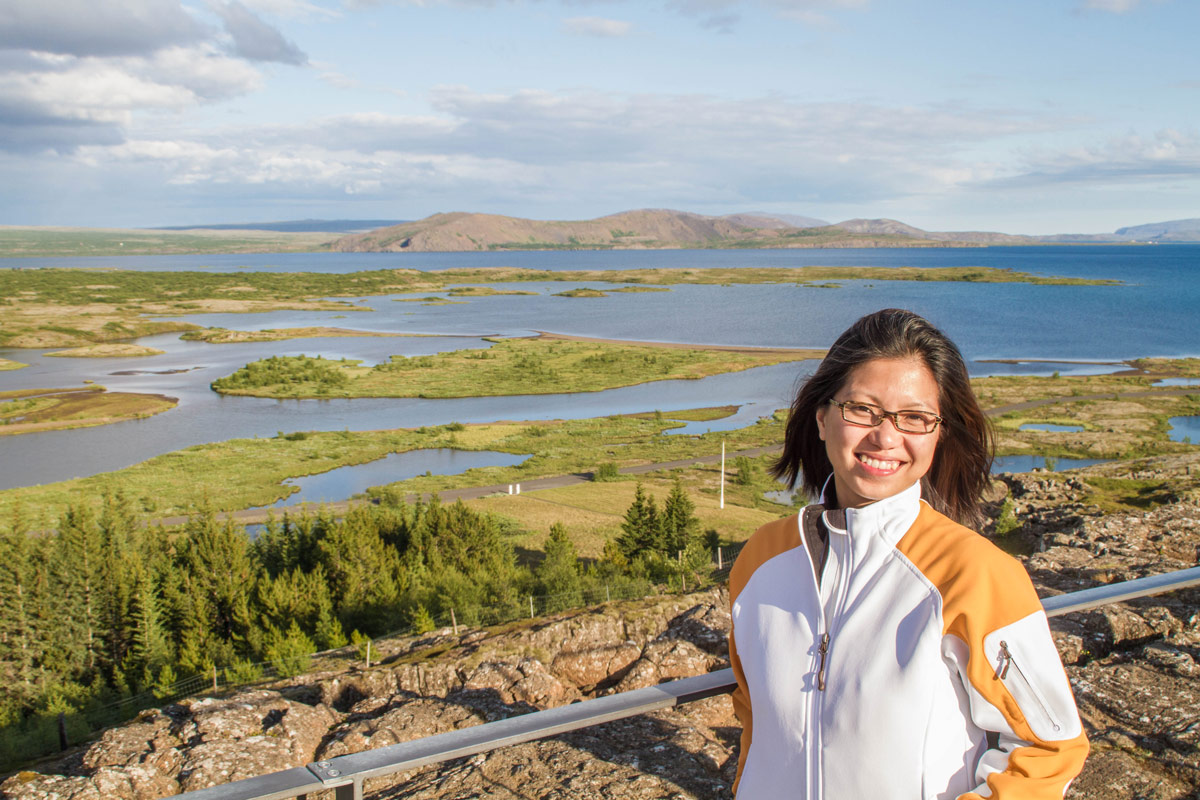 A woman smiles while standing at an overlook. Behind her are grasslands and lakes - Epic 14 Day Iceland Itinerary