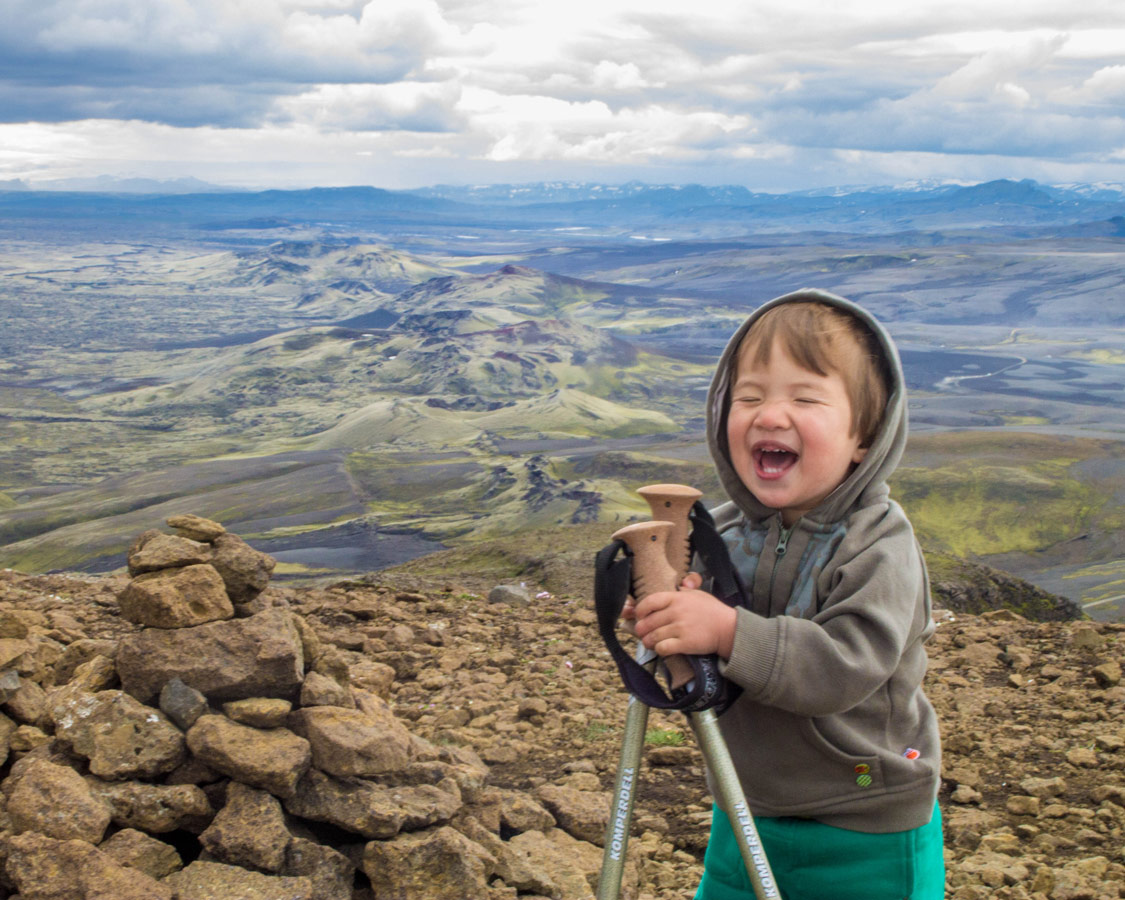 A young boy holding hiking poles laughs on a mountain top - An Epic 14 Day Iceland Itinerary