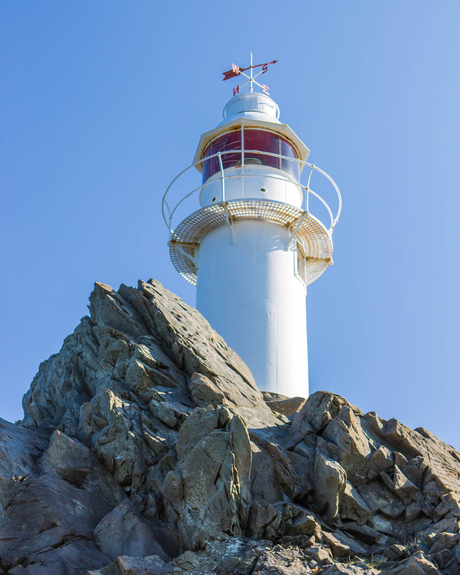 A white lighthouse with red accents posed on top of a rocky cliff - Newfoundland Viking Trail