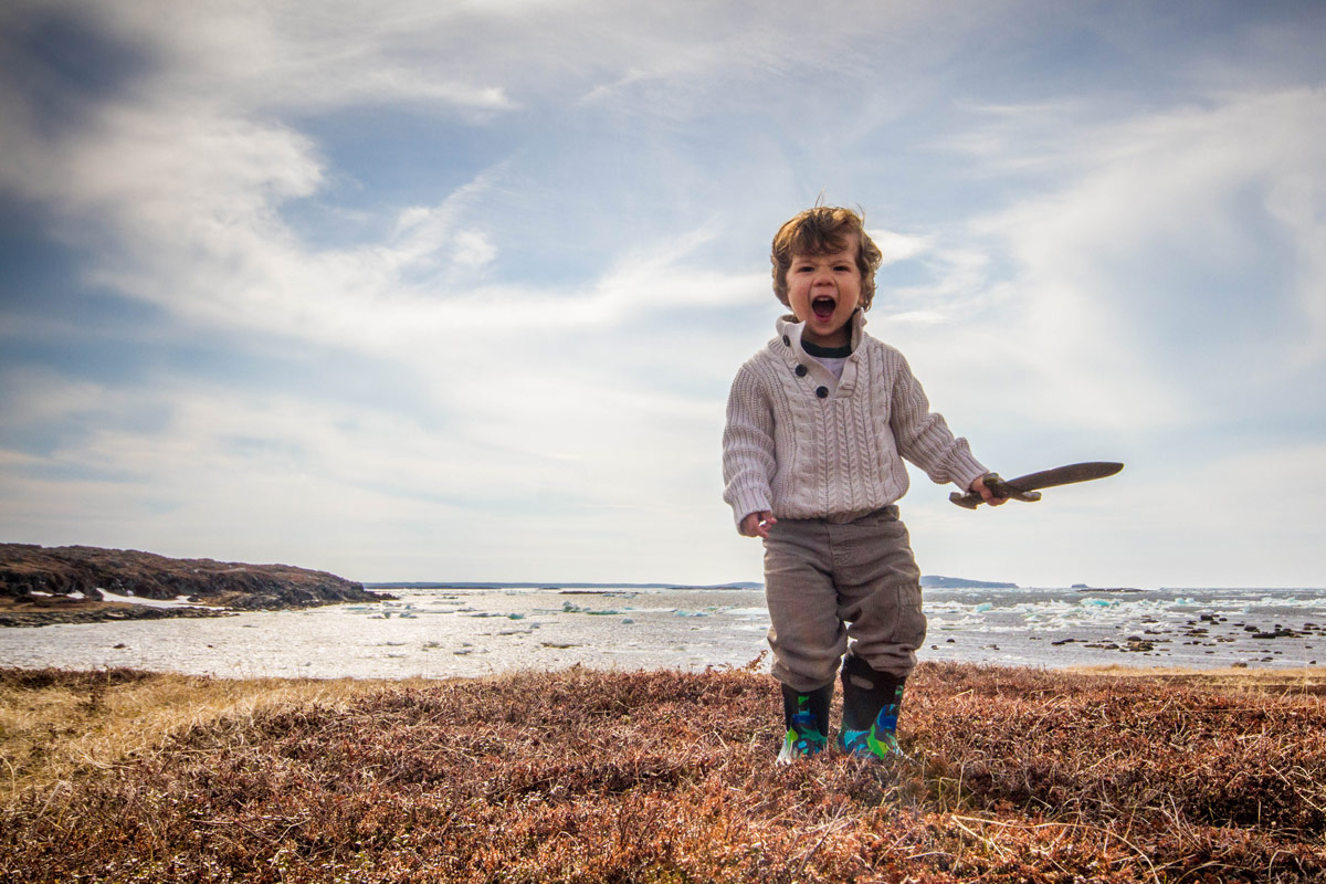 A young boy in a whole sweater, carrying a toy sword screams fiercely at a Viking village - Newfoundland Viking Trail