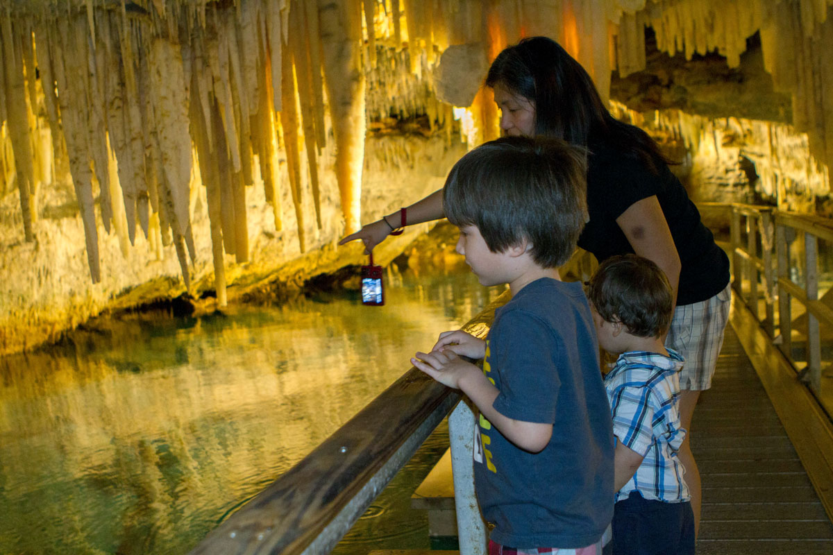 A mother points to rock formations inside a cave to two young boys - caves you can visit with kids