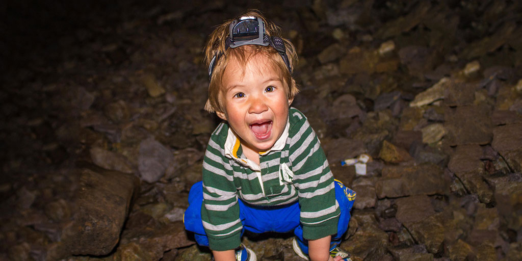 A toddler wearing a headlamp smiles happily inside a cave - caves you can visit with kids