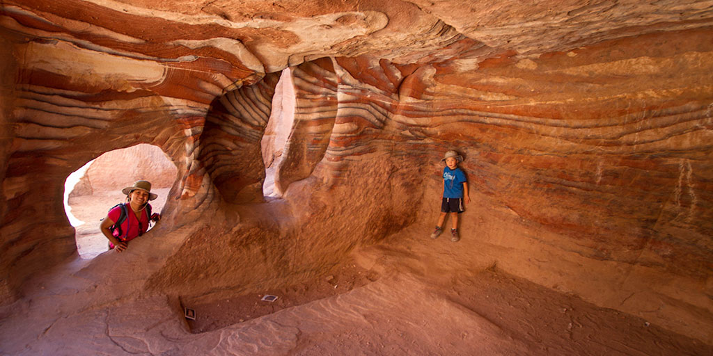 A young boy stands in a cave in Petra Jordan while his mother looks in from a window - caves you can visit with kids