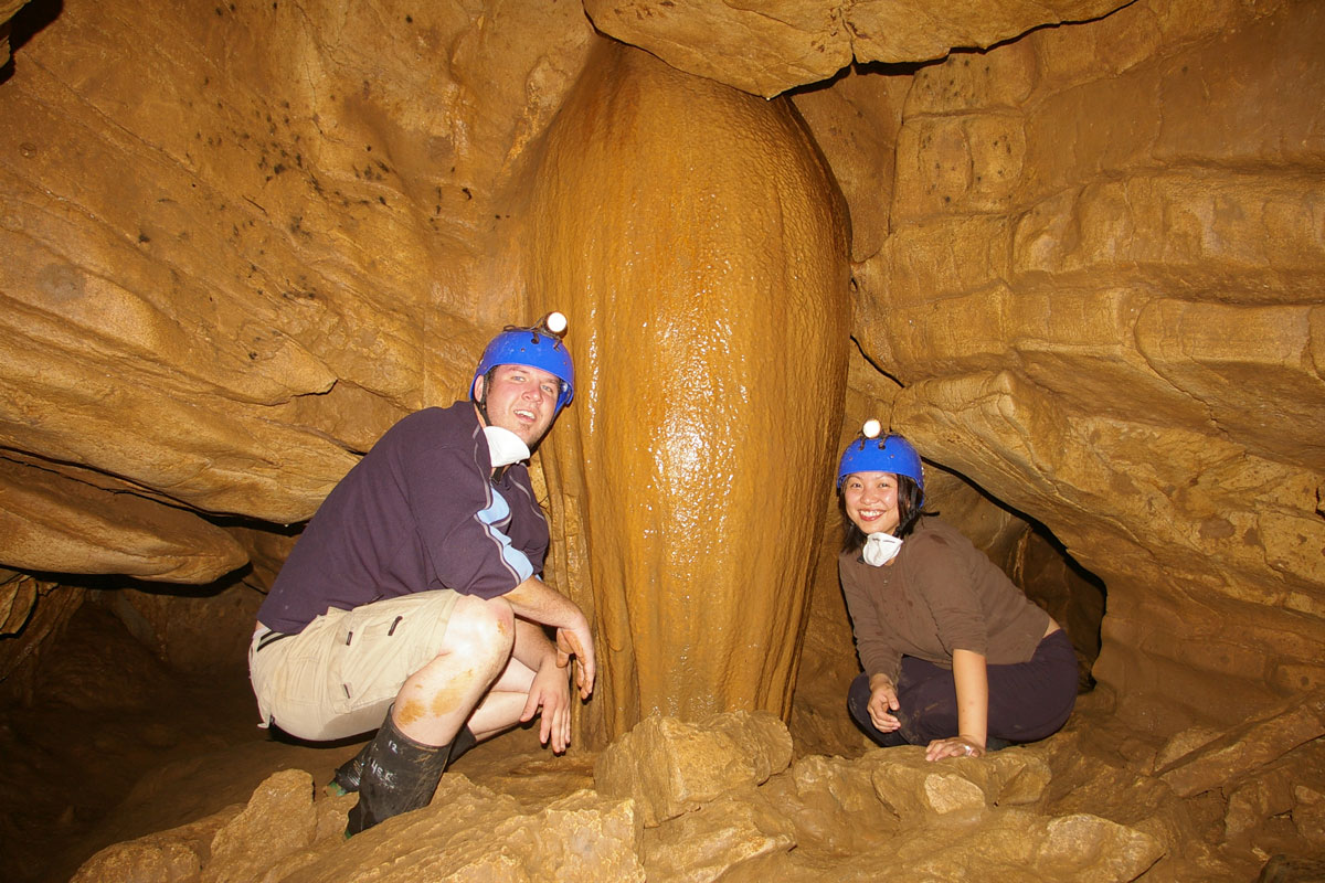 A man and woman wearing caving gear pose near a large rock formation - caves you can visit with kids