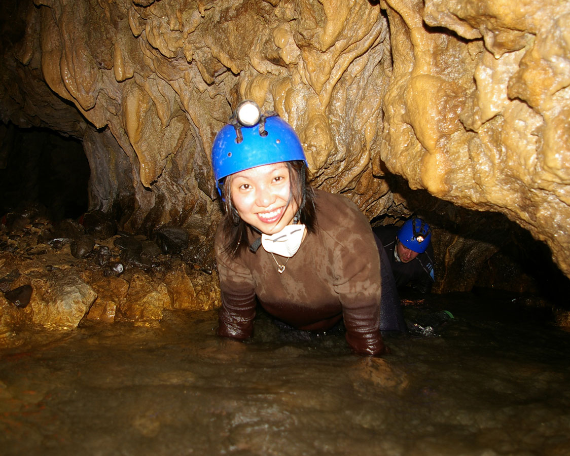 A woman wearing a hard hat and headlamp emerges from the water inside a cave - caves you can visit with kids