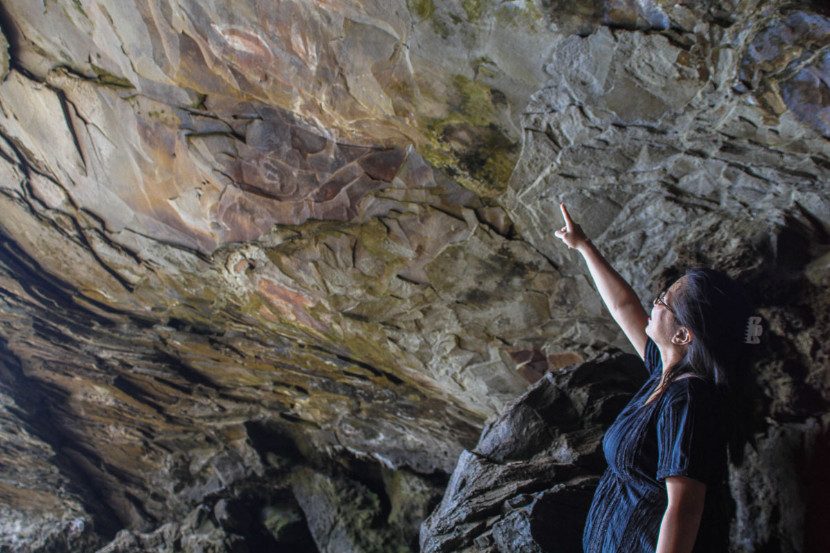 A woman points at paintings inside a sea cave on Easter Island - caves you can visit with kids