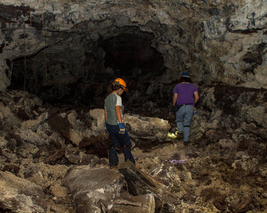 A woman wearing a headlamp explores a lava tube - caves you can visit with kids