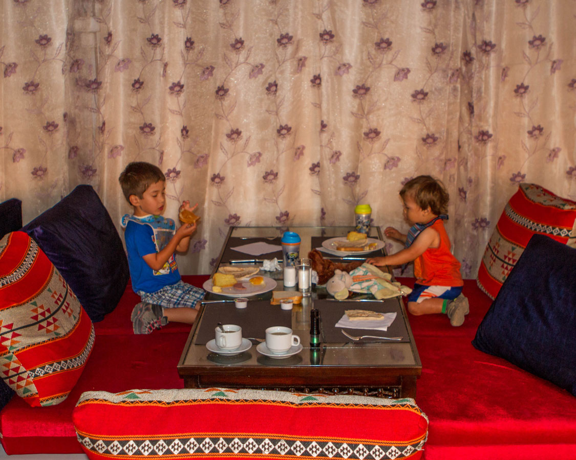 two young boys eat breakfast in a bedouin tent in the Wadi Rum Desert of Jordan - plan international family vacations