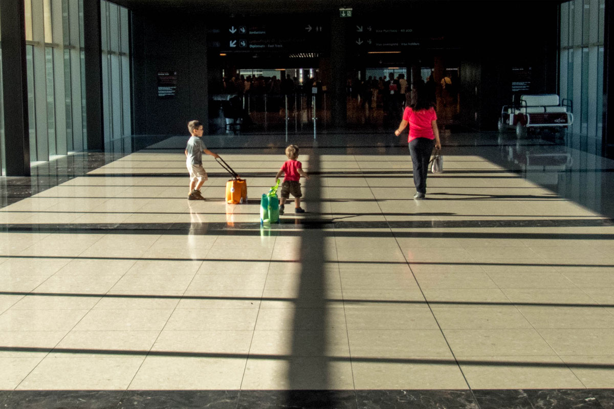 A mother and two young boys walk through an airport walkway - plan international family vacations