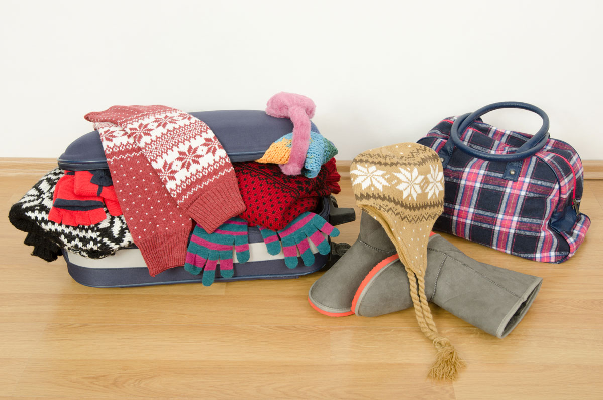 Luggage overflowing with winter clothes on a wood floor - plan international family vacations