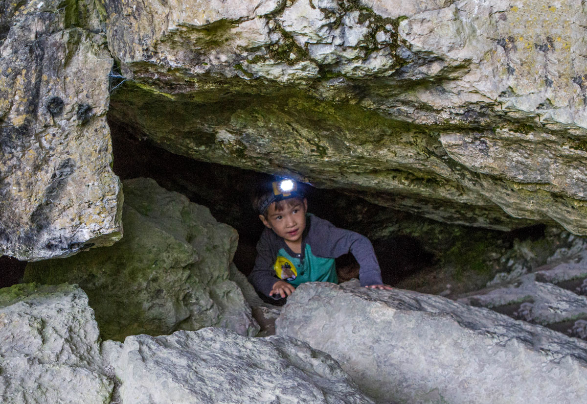 A young boy wearing a headlamp emerges from a cave in Ontario - caves you can visit with kids