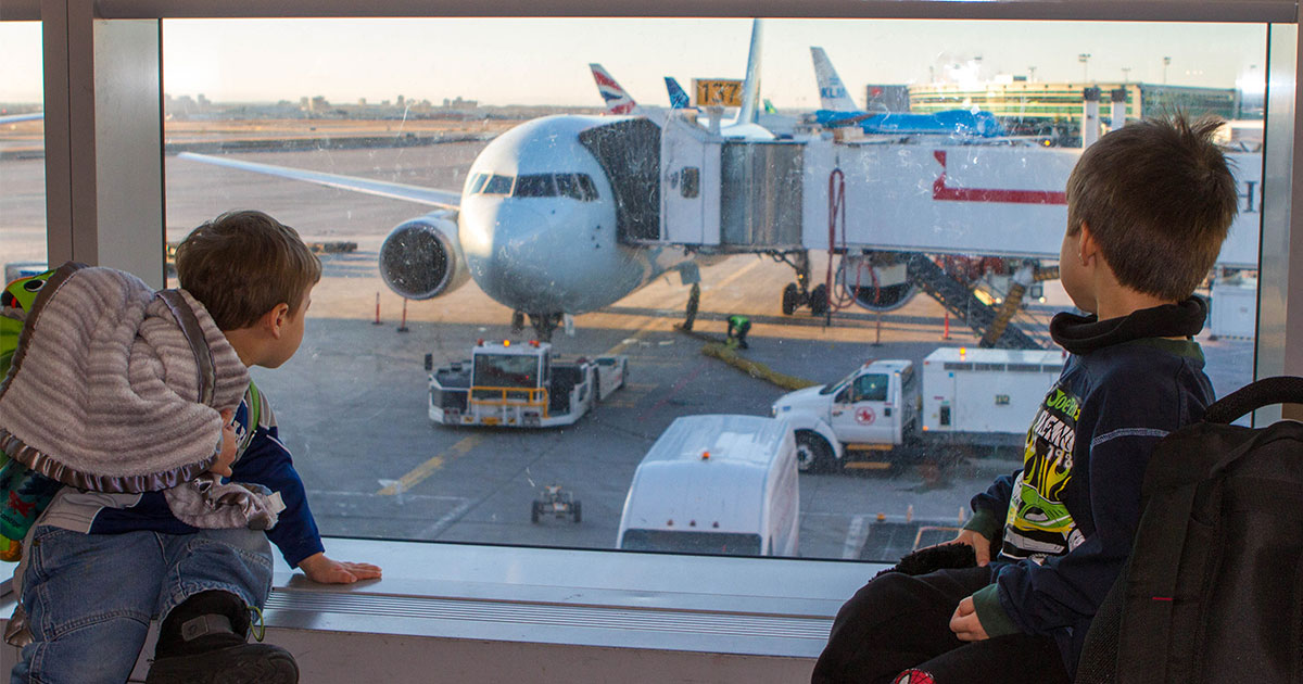 Two young boys watch planes out of an airport window - plan an international family vacation