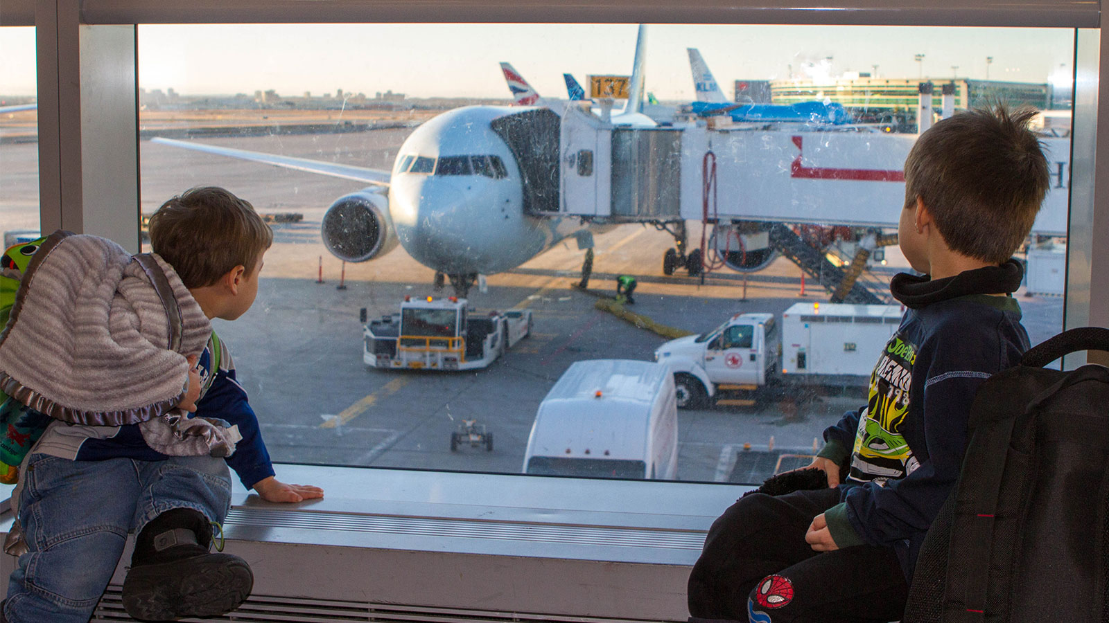 Two young boys watch planes out of an airport window - plan an international family vacation