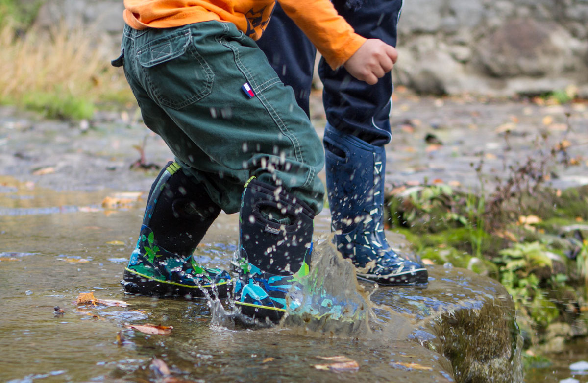Closeup of the feet of two young boys splashing in a stream - Bogs kids winter snow boots