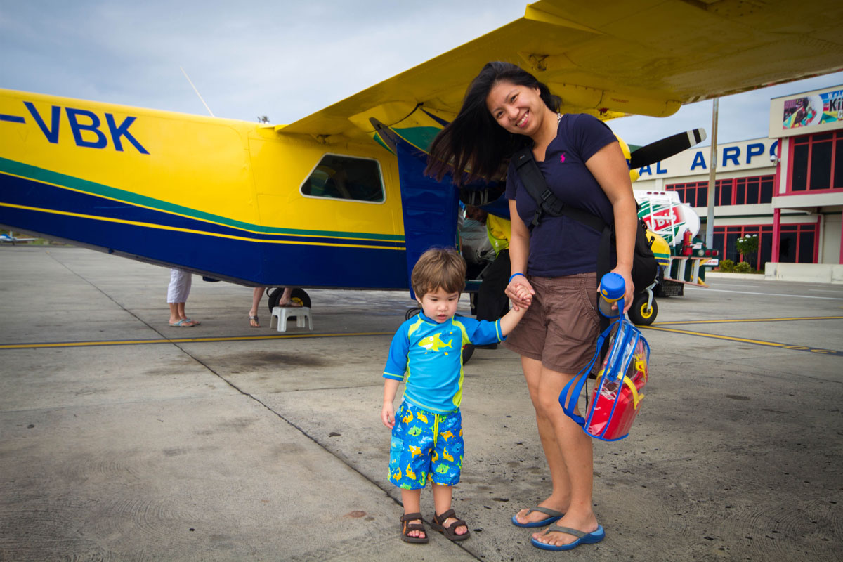 A woman an toddler son smile while boarding a small yellow airplane - Swimming with Turtles in the Tobago Cays