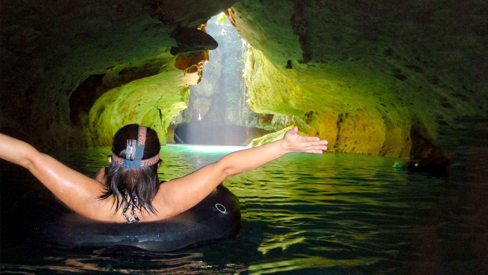 A woman in a tube floats towards a beautiful cave entrance with her arms outstretched