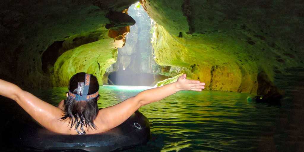 A woman in a tube floats towards a beautiful cave entrance with her arms outstretched