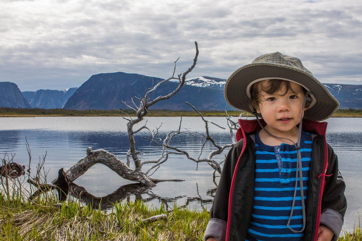 A young boy in explorer gear poses in front of Western Brook Pond in Newfounland