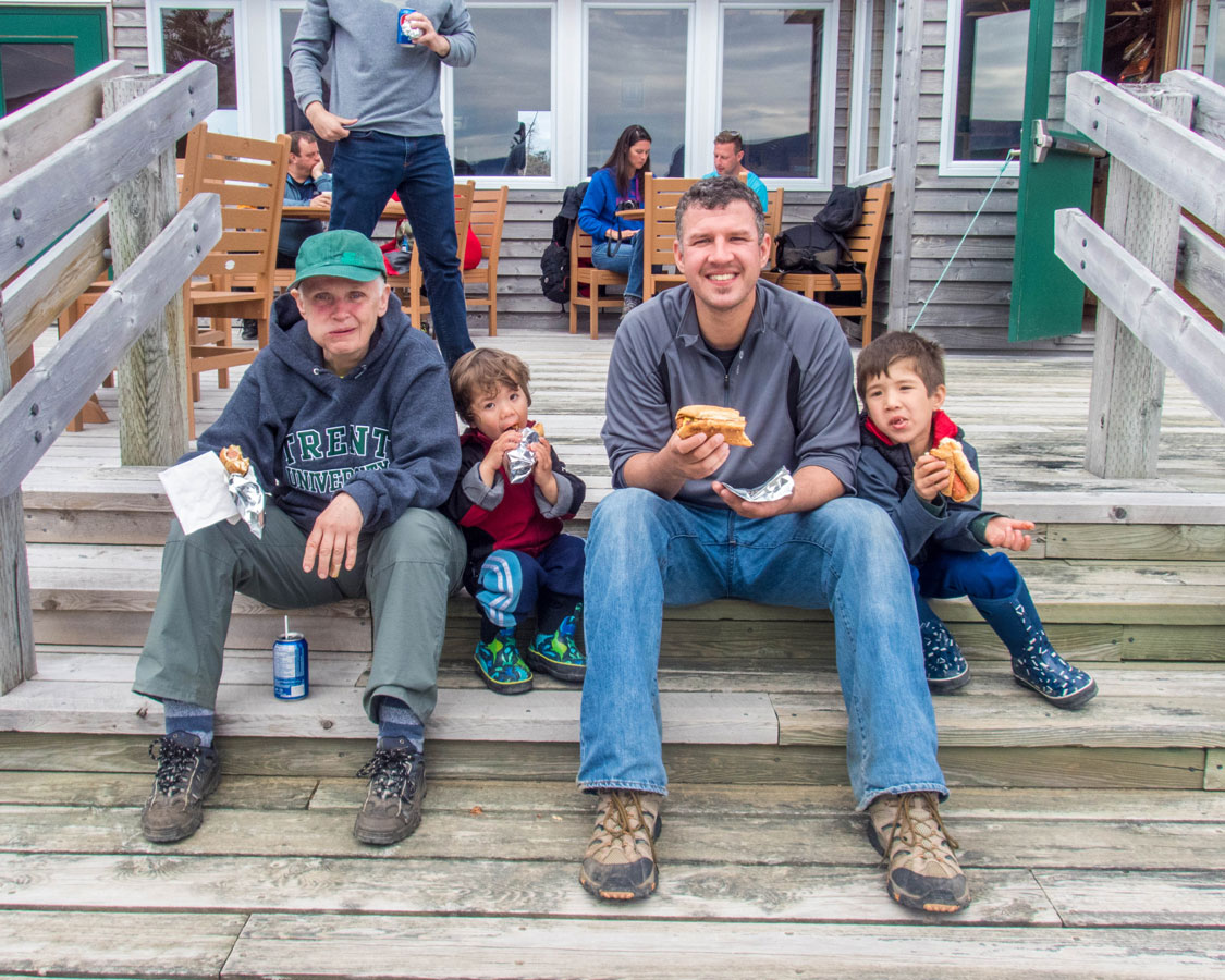 A grandmother, father and two young boys eat hot dogs on a set of stairs