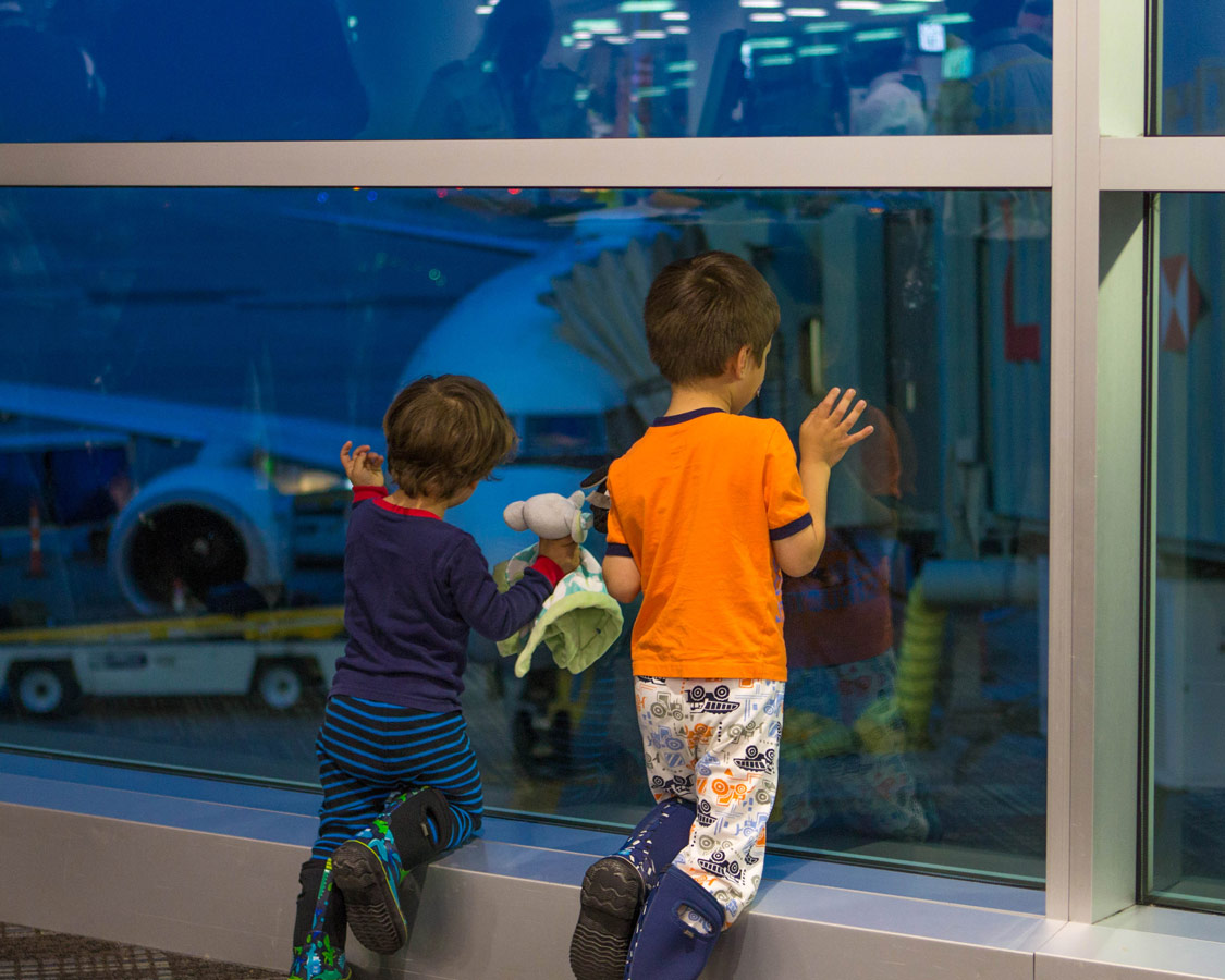 Two young boys stare out the window at an airport