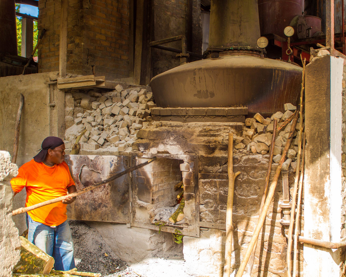 A Caribbean rum worker stokes a large antique boiler by hand at the River Antoine Rum Distillery in Grenada