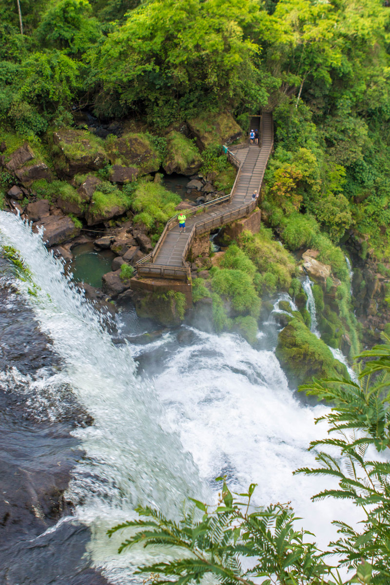 Looking over the edge of a coarsing waterfall. A small catwalk is beneath it with visitors watching the watefall