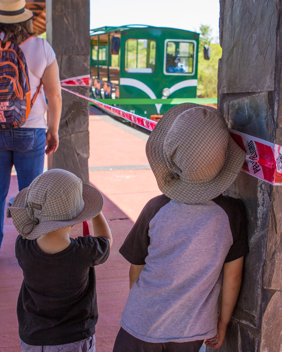 Two boys lean against a post as a small train comes into the station at Iguazu Park Visitor Centre in Argentina