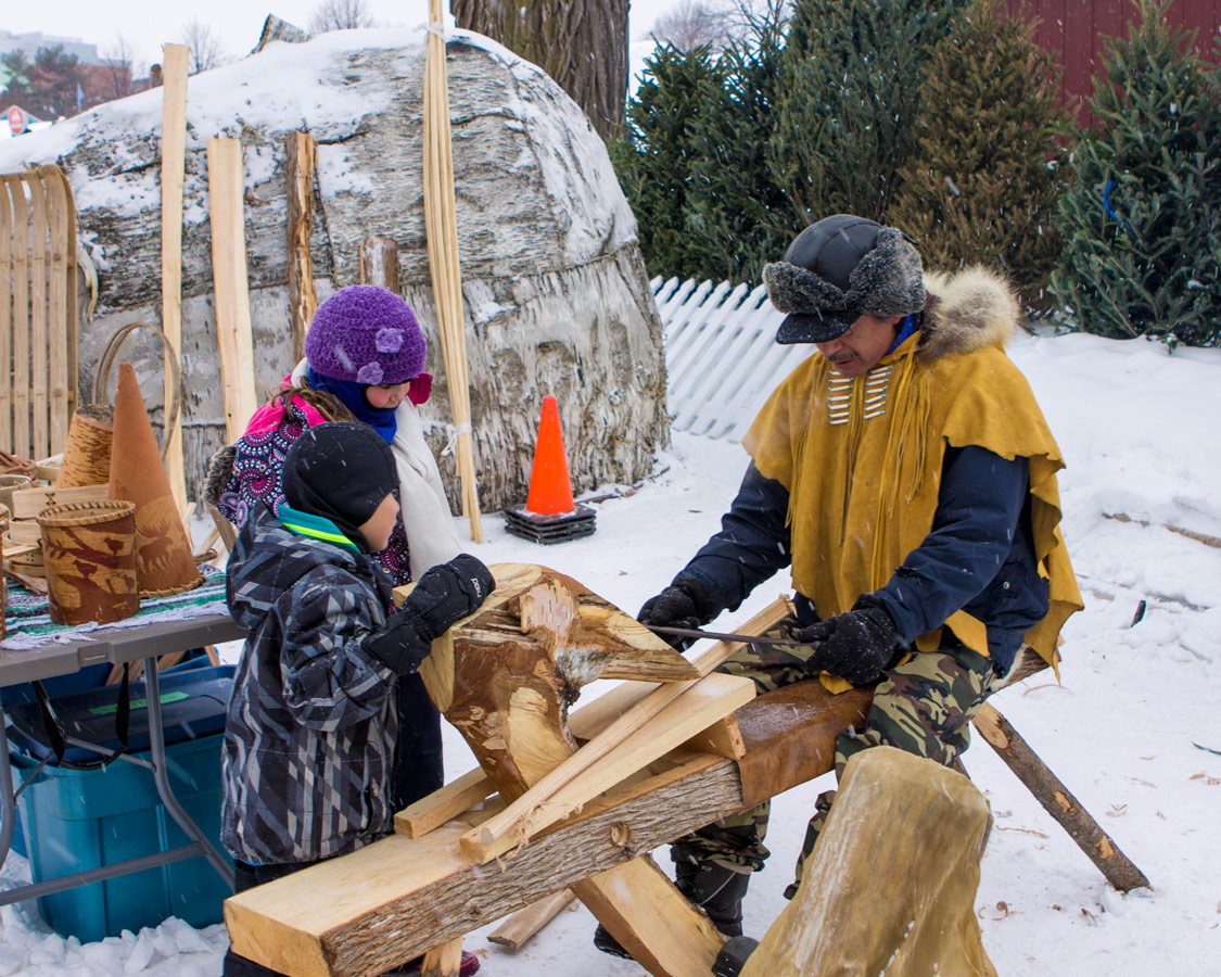 Boys watching wood get carved the traditional way.