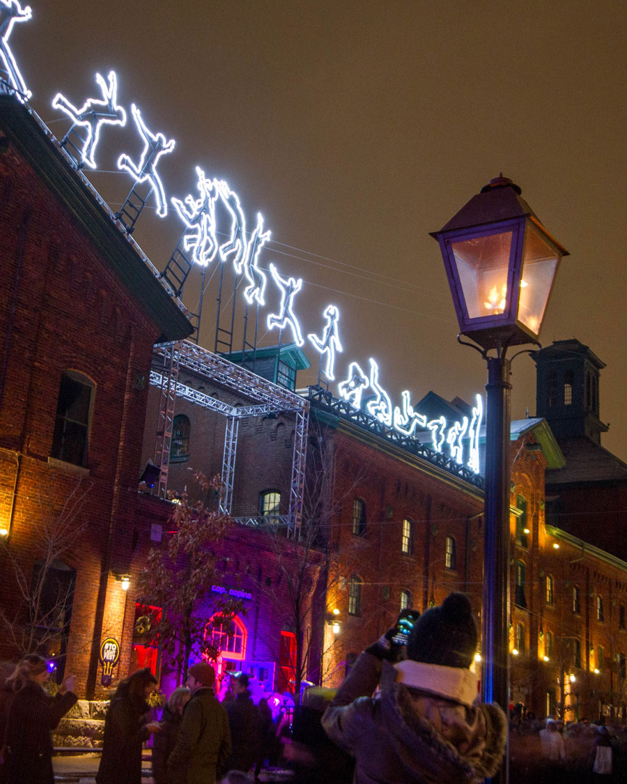 Flame lanterns in the foreground and light art of a parkour artist in the background of the Distillery District during the Toronto LightFest