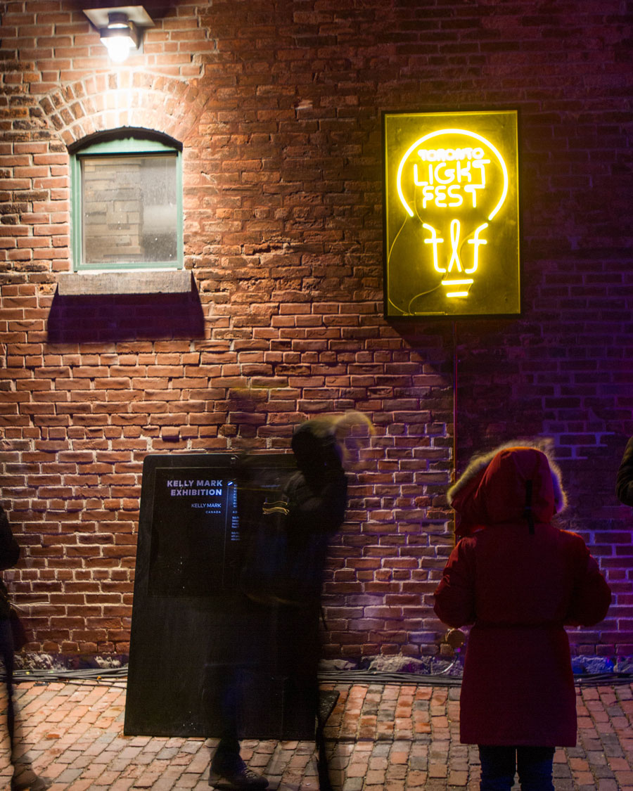 A woman in a red Canada Goose Jacket looks at Light art of the Toronto Lightfest in the Distillery District