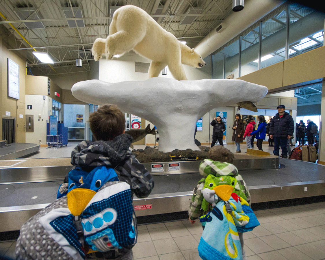Two boys look at a display of a polar bear chasing a seal on an iceberg at the Yellowknife Northwest Territories airport while they look for things to do in Yellowknife