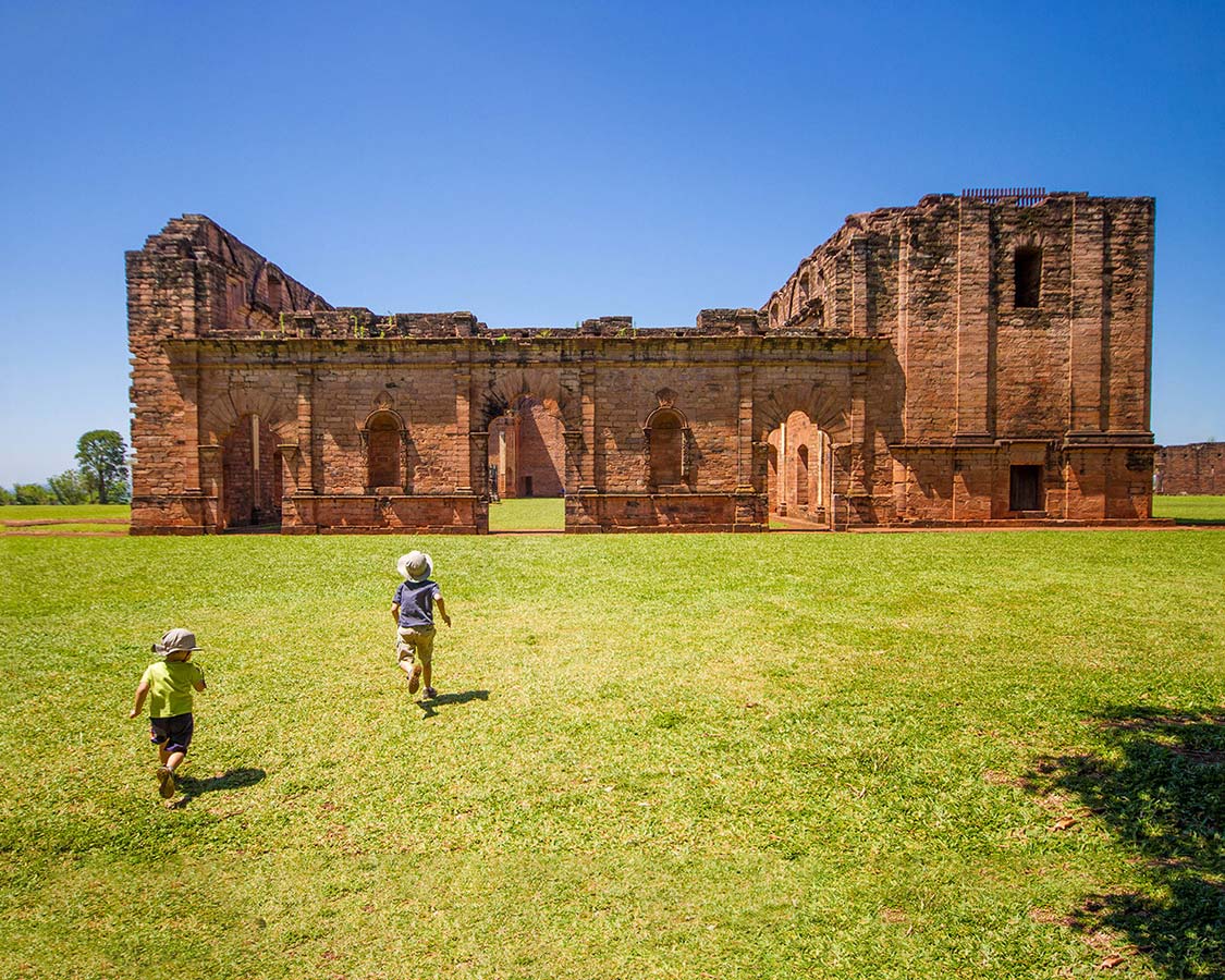 Two young boys running towards the ruins of a Jesuit Mission in Paraguay