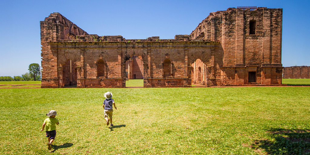 Two young boys running towards the ruins of a Jesuit Mission in Paraguay