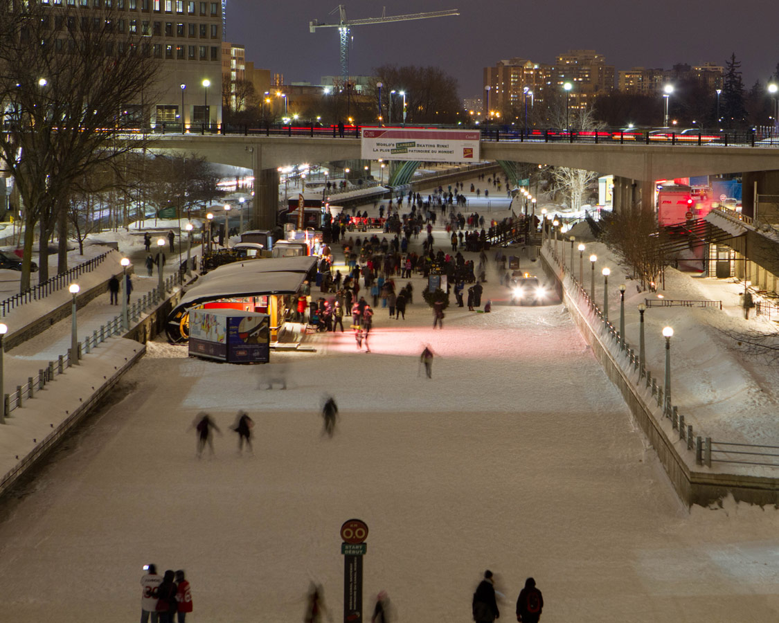 View of Rideau Canal Skateway filled with ice skaters during the Winterlude festival at night.