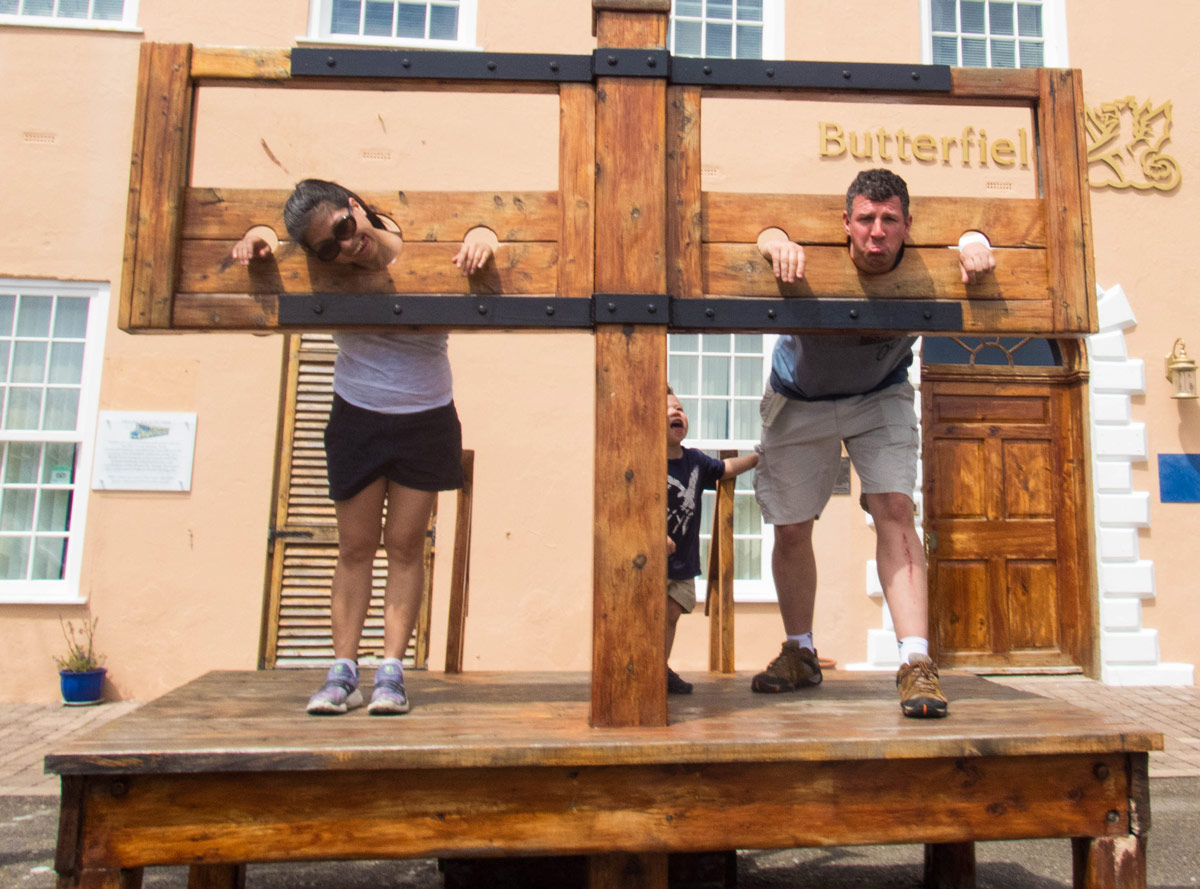 Woman and man pose in a pillory in the town square in St George Bermuda.