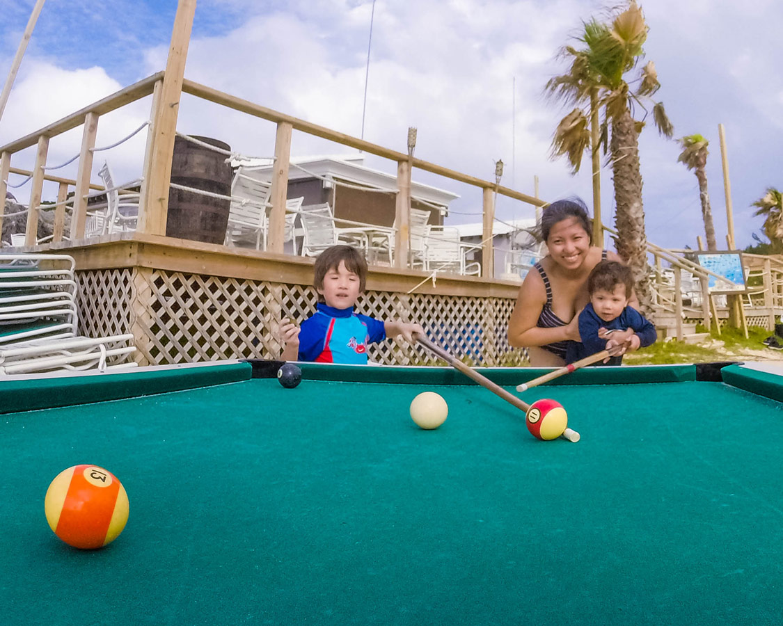 Woman and two boys playing outdoor billiards in Tobacco Bay, St George Bermuda.