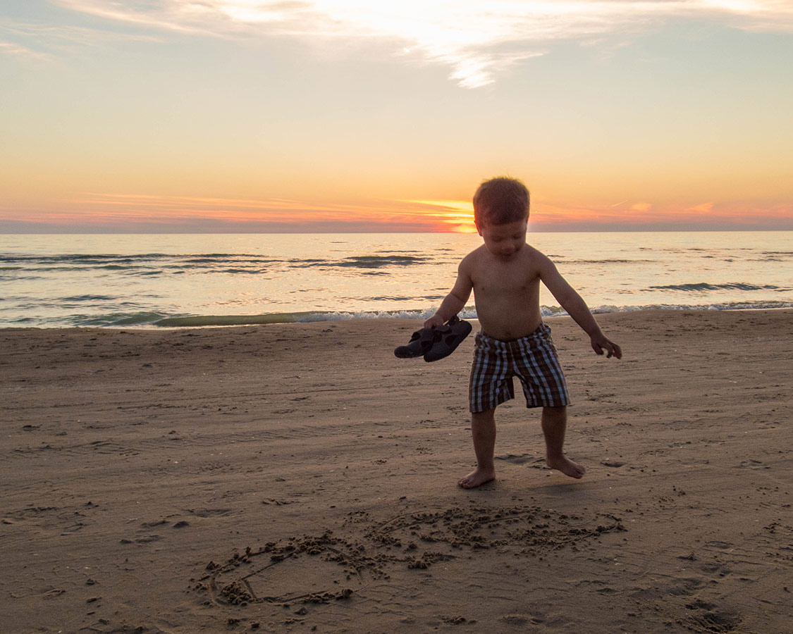 Boy tries to write in the sand during sunset at Sauble Beach.
