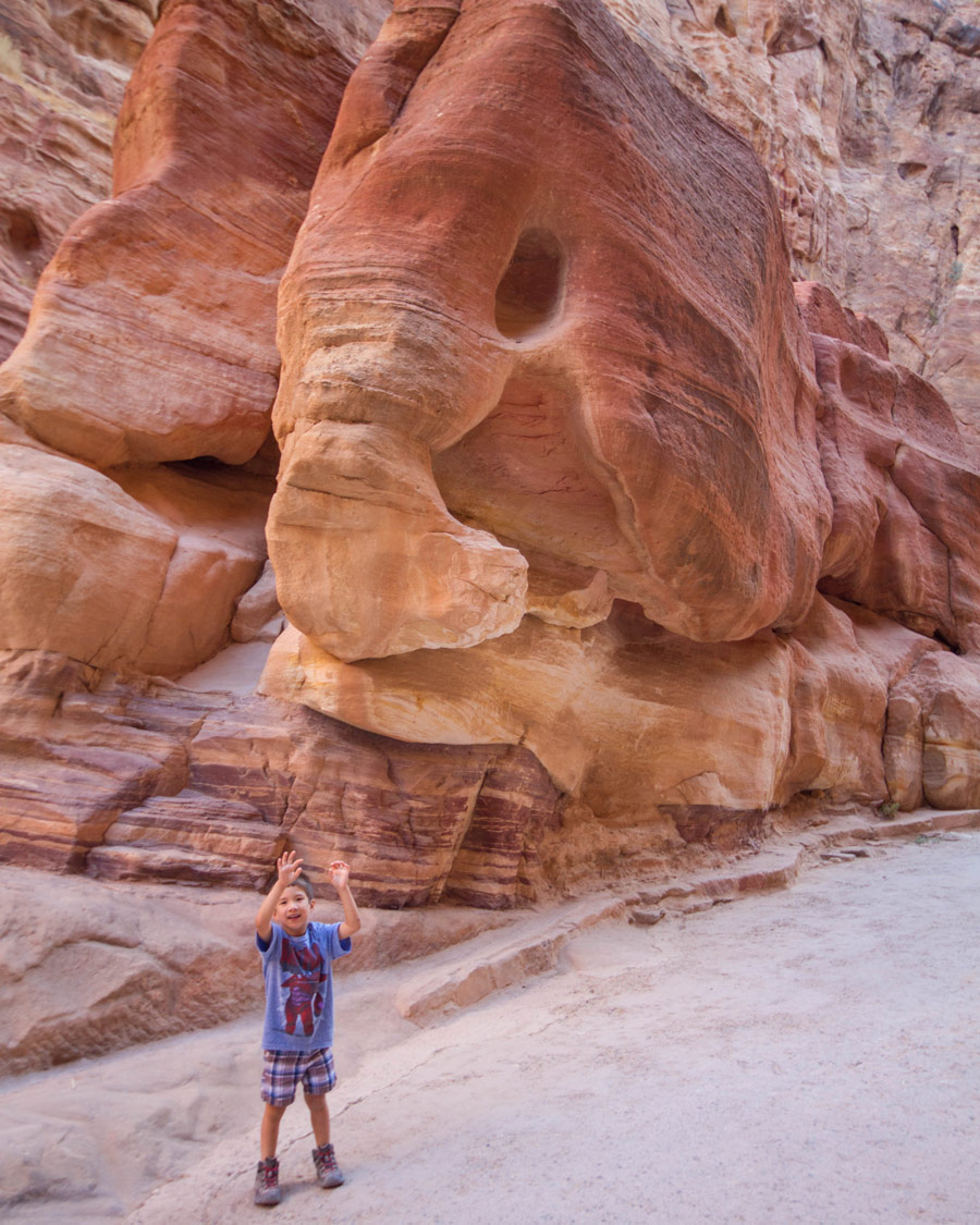 A young boy stands under a rock shaped like an elephant in the siq on the way to Petra Jordan