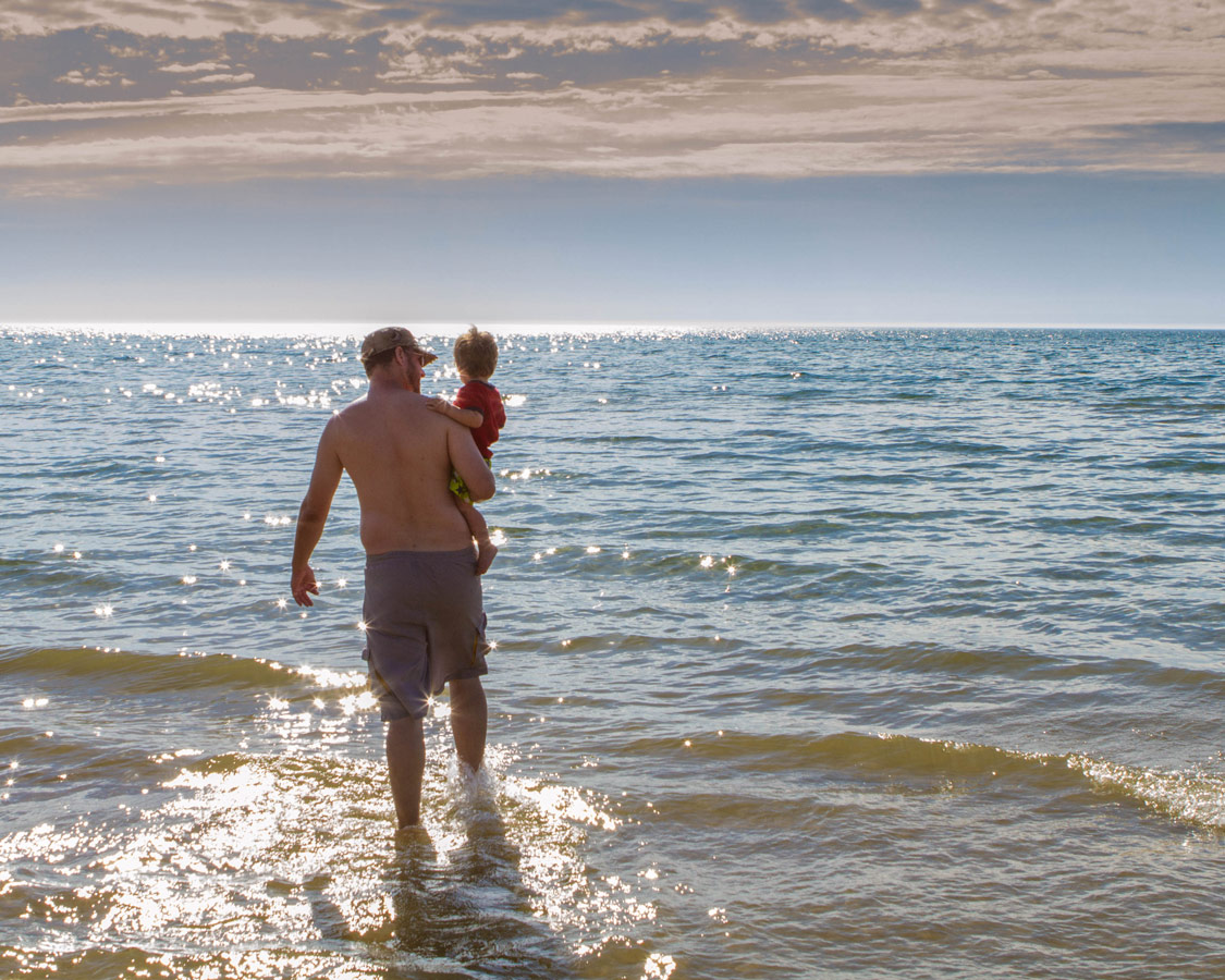 Father carries son into the waters of Sauble Beach, Ontario.