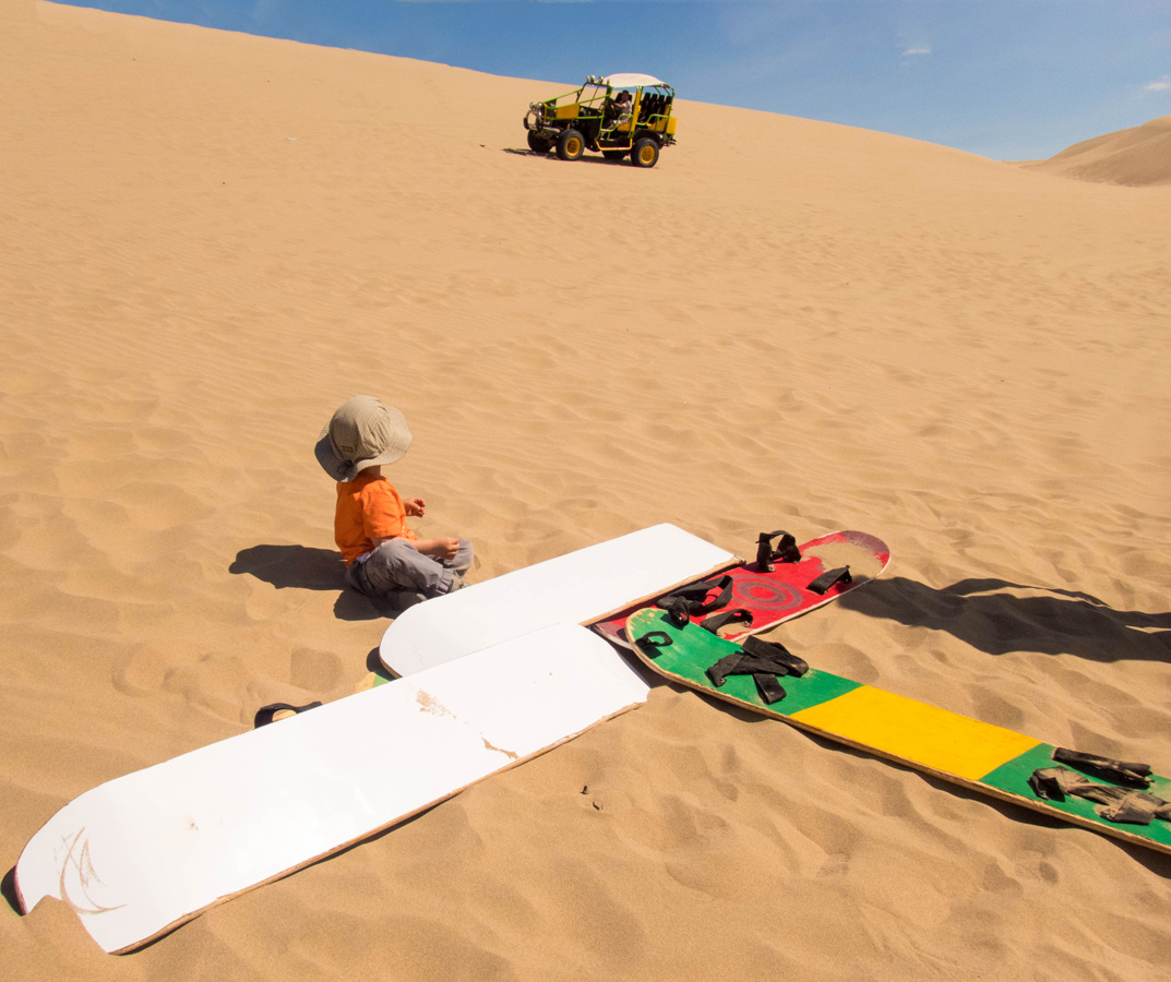 A toddler sits with sandboards in Peru while waiting for a dune buggy to pick him up