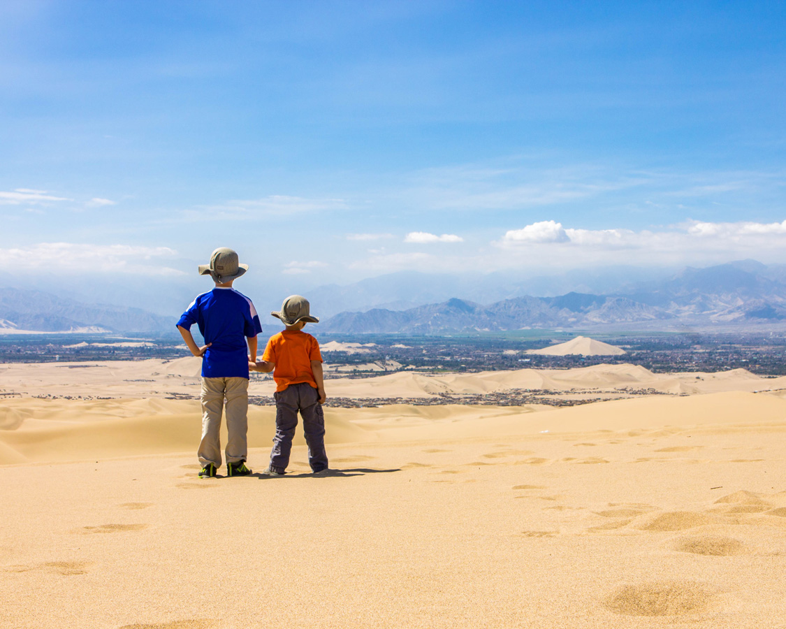 Two young boys hold hands while looking out over the town of Ica from the desert near Huacachina as the go sandboarding with kids in Peru