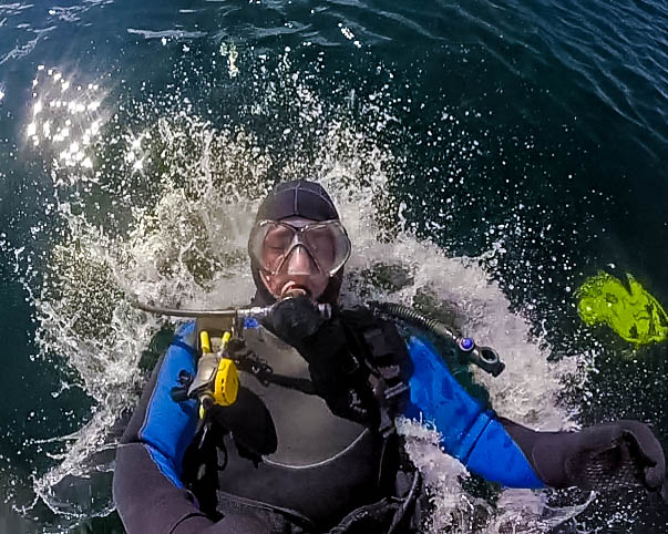 A SCUBA diver splashes backwards into the water as seen from above