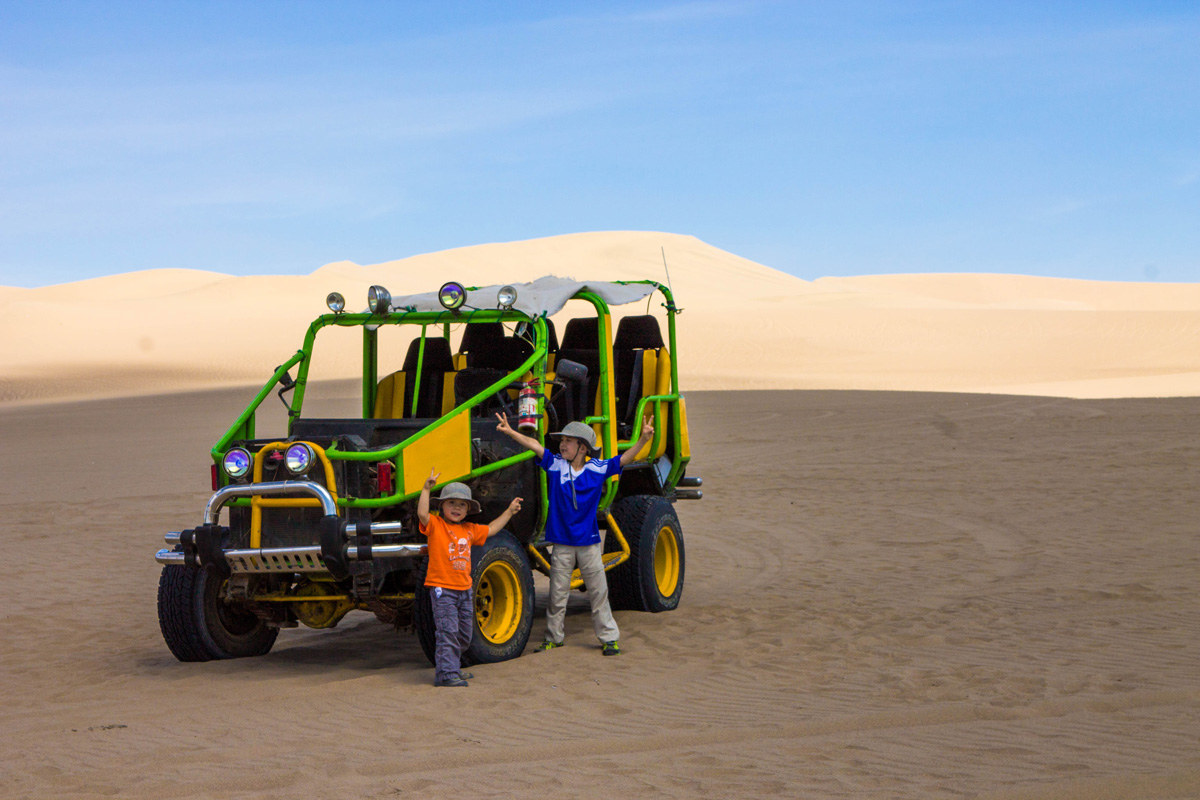 Two young boys stand next to a massive dune buggy as they go Sandboarding in Huacachina Peru