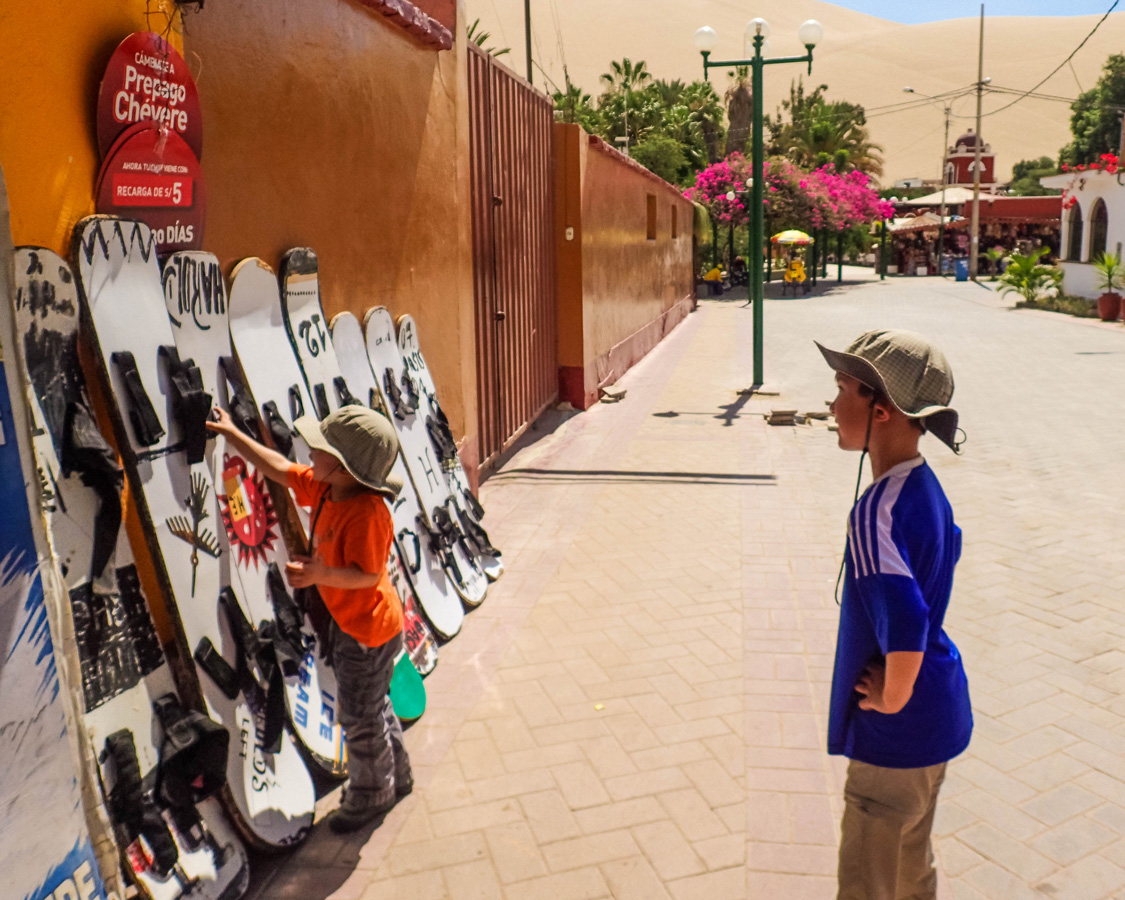 Young boy looks at sandboards on a street as he prepares to Sandboard in Huacachina Peru with Kids