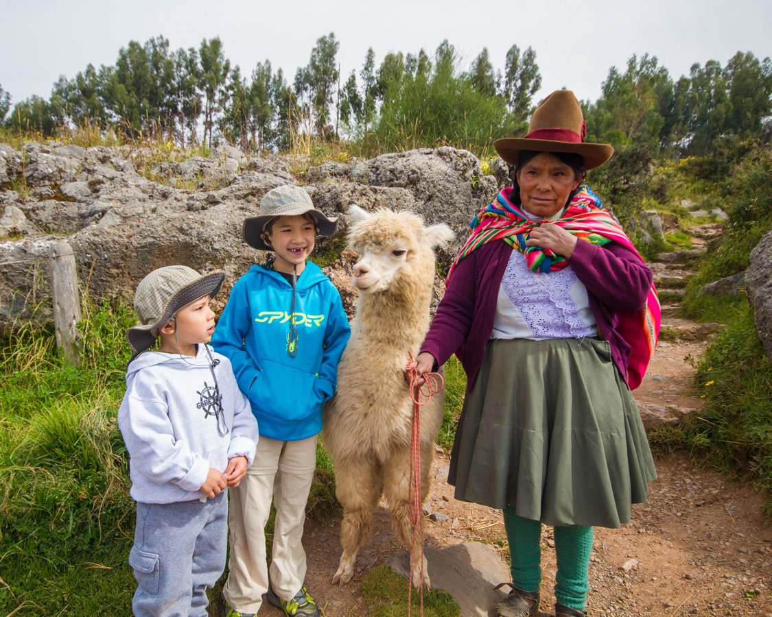 A Peruvian woman introduces two boys to her llama in Sacsayhuaman as they head to the ChocoMuseo in Cusco Peru