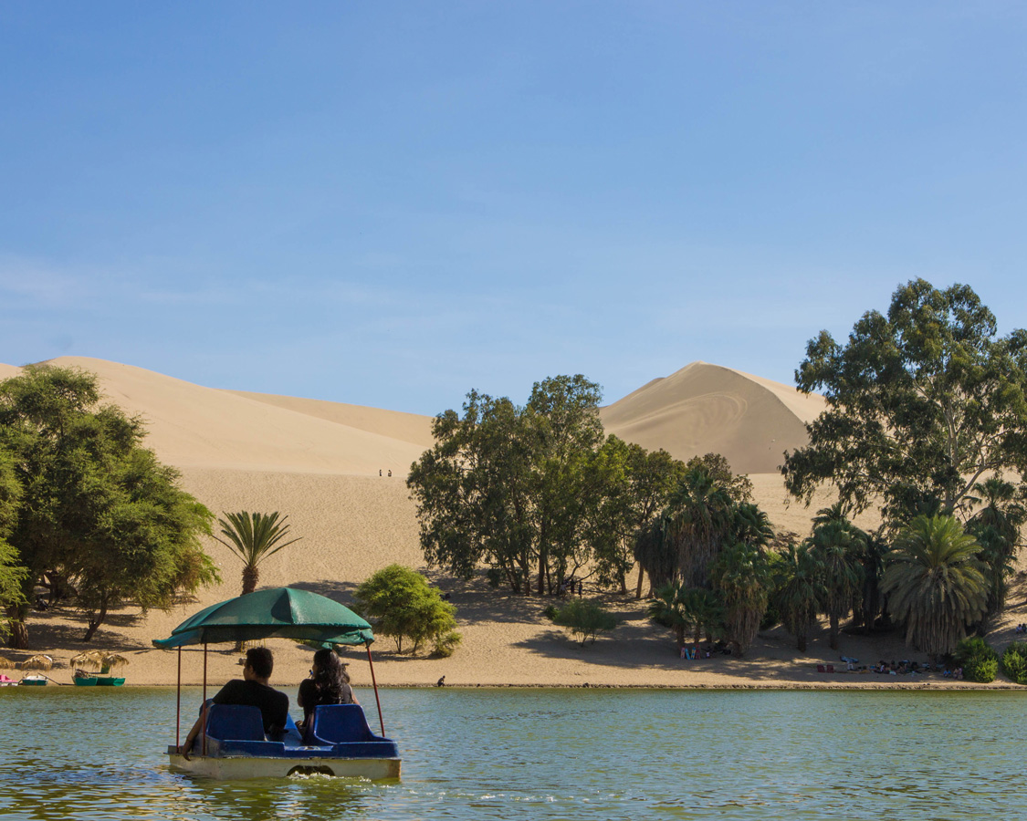 Boaters explore the oasis in Huacachina Peru, a perfect place to relax while sandboarding with kids in Peru