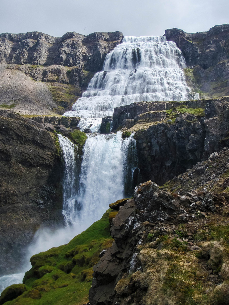 A tall triangular shaped waterfall cascading down a rock cliff in Iceland's Westfjords